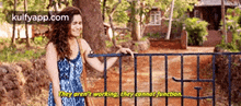 a woman in a blue dress is standing next to a fence and talking to a man .