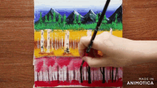 a hand is holding a brush in front of a painting of trees and mountains made by animatica