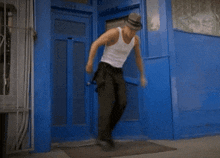a man in a white tank top and black pants dancing in front of a blue door