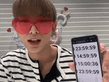 a man wearing red heart shaped sunglasses is holding a cell phone with the time 23:59:59 on it