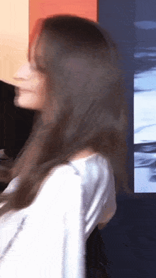 a woman with long hair is standing in front of a wall with a picture on it .