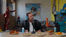 a man wearing headphones sits at a table with plates of food and a can of lucky strike