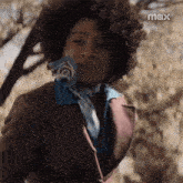 a woman with curly hair wearing a suit and scarf is standing in front of a tree .
