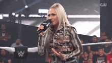 a woman is speaking into a microphone in front of a crowd with a cw logo in the background