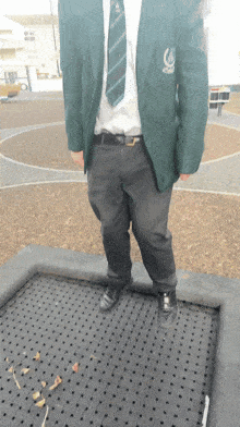 a man wearing a green jacket and tie is standing on a trampoline