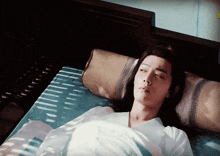 a man with long hair is laying on a bed with a greek key pillow