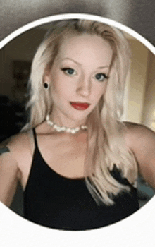 a woman wearing a black tank top and a pearl necklace is taking a selfie .