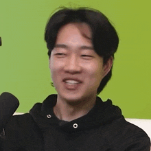 a young man in a black hoodie is smiling and talking into a microphone