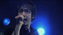 a man singing into a microphone in front of a blue light