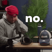 a man wearing a red hat is sitting at a desk with the word no written above him