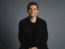 a man in a black jacket and black shirt smiles for the camera