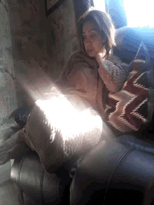 a woman is sitting on a couch with a blanket and a pillow