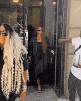 a woman in a black dress and sunglasses is walking down the street