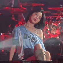 a woman is sitting on a stage with a drum set in the background