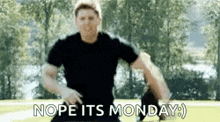 a man in a black shirt is running in a park with the words `` nope its monday '' written on the screen .