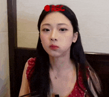 a woman with long black hair is sitting in front of a wall with a red rec sign on it