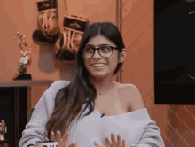 a woman wearing glasses and a sweater is sitting in front of a television .