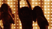three women are dancing in front of a wall with lights