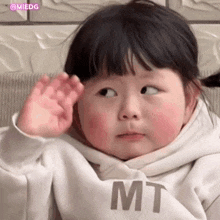 a little girl wearing a white sweatshirt with the word mt on it is sitting on a couch .