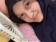 a woman wearing a hijab is laying next to a fan and the word hahaha is on the bottom right