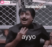 a man is sitting in front of a chain link fence and making a funny face and saying ayo .