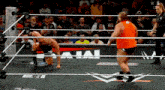 a wrestler in an orange shirt is kneeling down in the ring