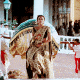 a woman in a gold and black saree is standing in front of a fence