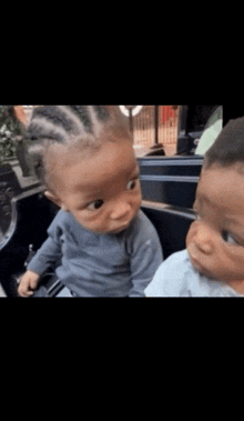 two babies are sitting next to each other in a car and one is making a funny face