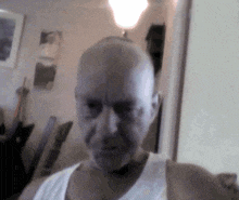 a bald man wearing a white tank top is taking a selfie