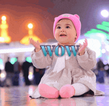 a baby wearing a pink hat and pink socks is sitting in front of a sign that says wow