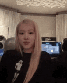 a woman with long blonde hair is wearing a black shirt in a room with a computer .