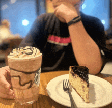 a person is sitting at a table with a starbucks drink and a piece of cheesecake
