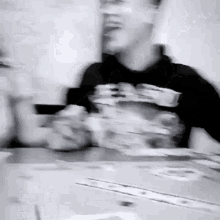 a blurry black and white photo of a man sitting at a table with cards .