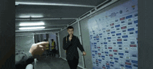 a man in a black suit stands in front of a wall that has a lot of advertisements on it