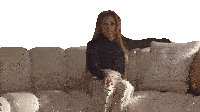 a woman sits on a white couch with a pillow that has a square pattern on it
