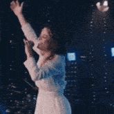 a woman in a white dress is singing into a microphone while standing on a stage .