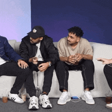 a group of men are sitting on a couch and one of them is wearing a hat that says ' nyc ' on it