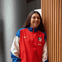 a woman wearing a red , white , and blue nike jacket is smiling .