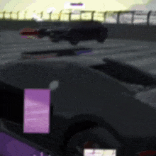 a black car is driving down a race track with a purple square in the foreground