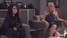 two women are sitting on a couch with peacock written on the bottom