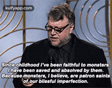 a man is giving a speech in front of a microphone while wearing glasses and a black shirt .