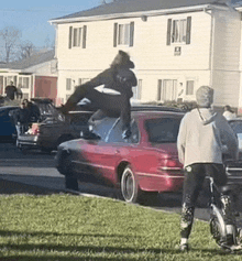 a man is doing a trick on top of a red car while another man looks on .