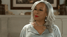 a woman with gray hair and red lipstick is wearing earrings and a necklace