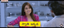 a woman in a pink plaid shirt is talking to a man in a kitchen with the words aditya music on the bottom left