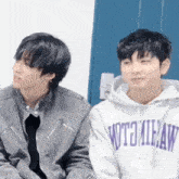 two young men are sitting next to each other in front of a blue door . one of the men is wearing a hoodie .