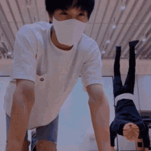 a man wearing a mask is doing push ups in a room while another man stands behind him .