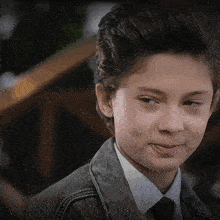 a young boy wearing a jacket and tie looks to his left