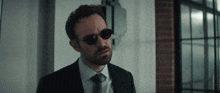 a man in a suit and tie wearing sunglasses looks at the camera