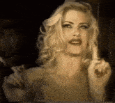 a blonde woman is holding a cigarette in her hand and pointing at the camera .