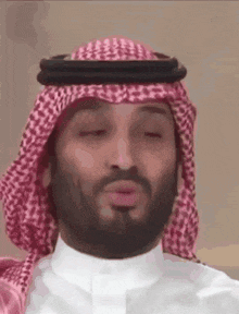 a man with a beard wearing a keffiyeh and a white shirt is making a face .